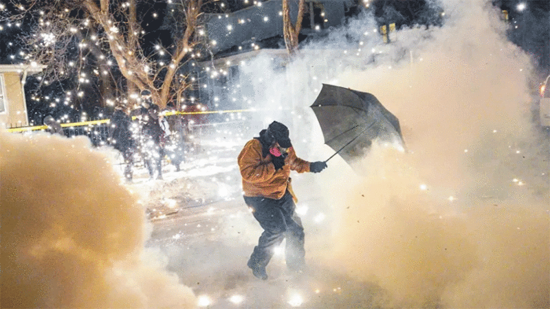 A protesting community member attempts to protect themselves as federal agents fire munitions and pepper balls in north Minneapolis, Minnesota, on 14 January 2026.
